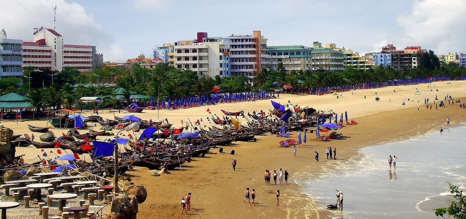Thuyền đánh cá xếp dọc bãi cát biển Sầm Sơn với hàng khách sạn phía sau, Thanh Hóa, Việt Nam.